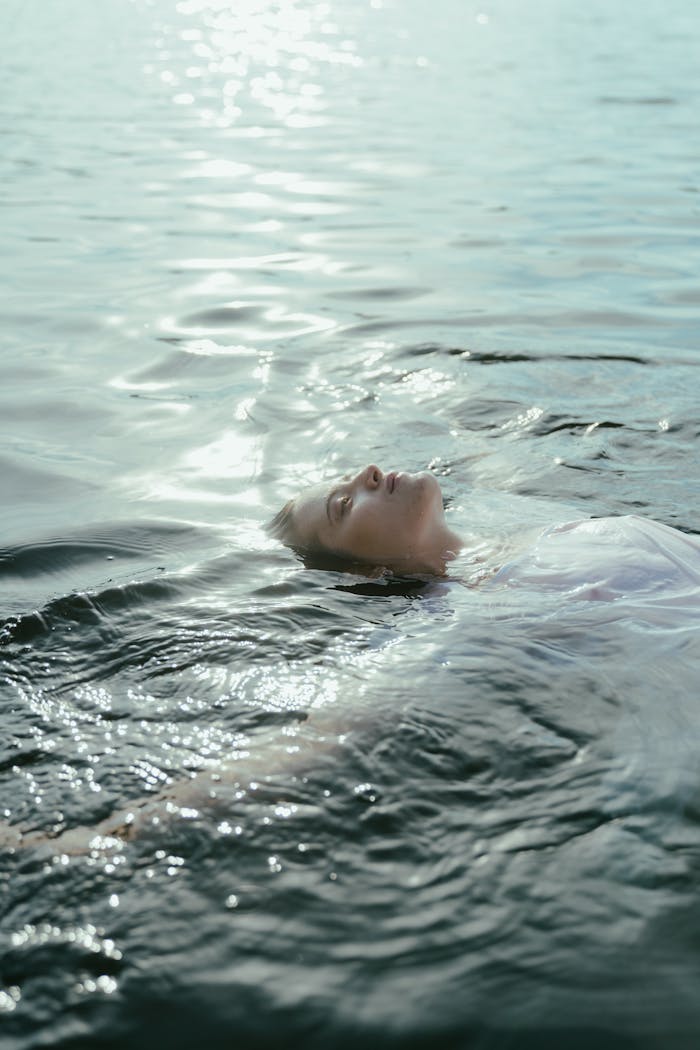 A peaceful scene of a woman in a white dress floating on a serene lake during daytime, capturing tranquility and freedom.