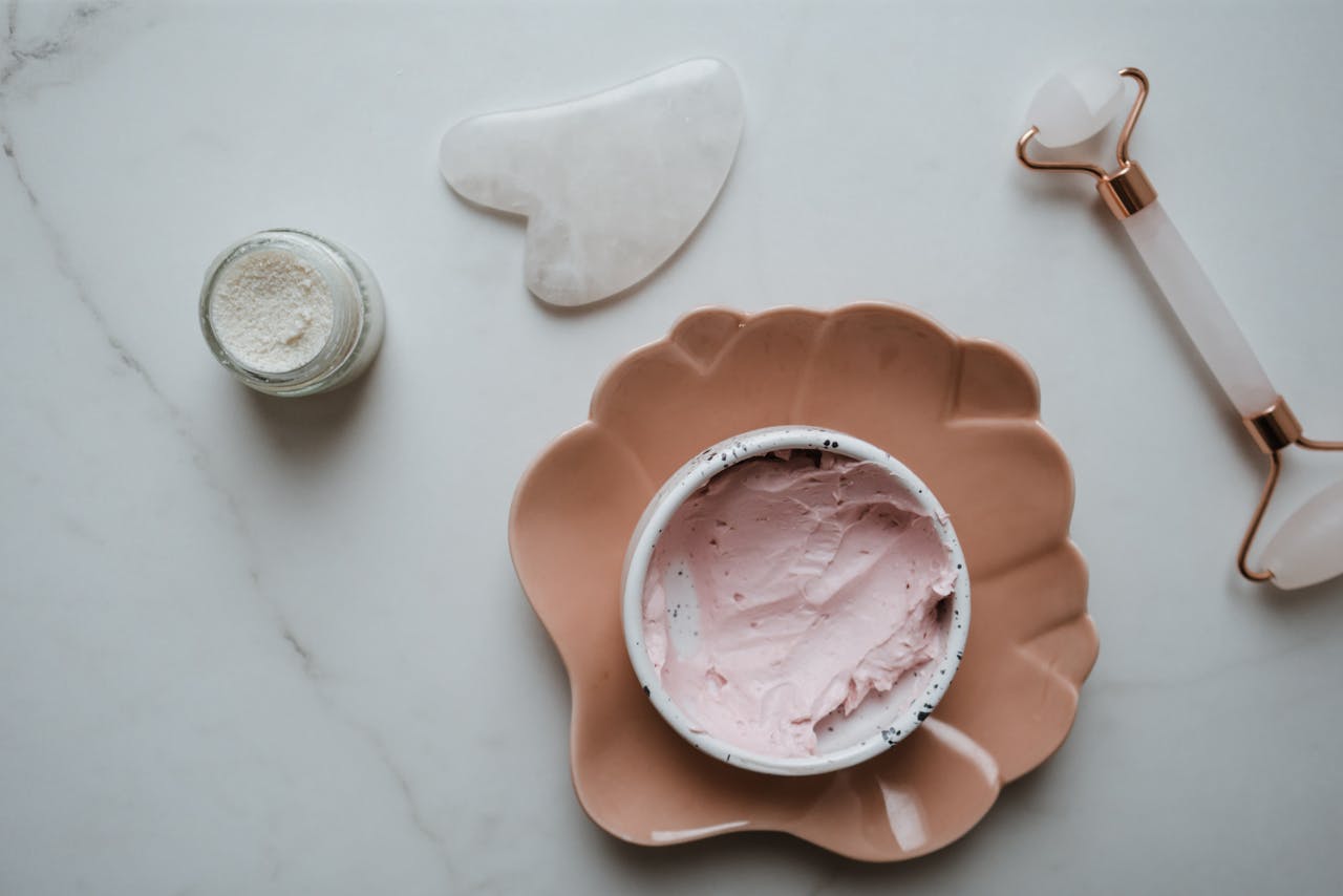 Elegant top view of skincare essentials including cream, gua sha, and roller on marble surface, perfect for beauty concepts.